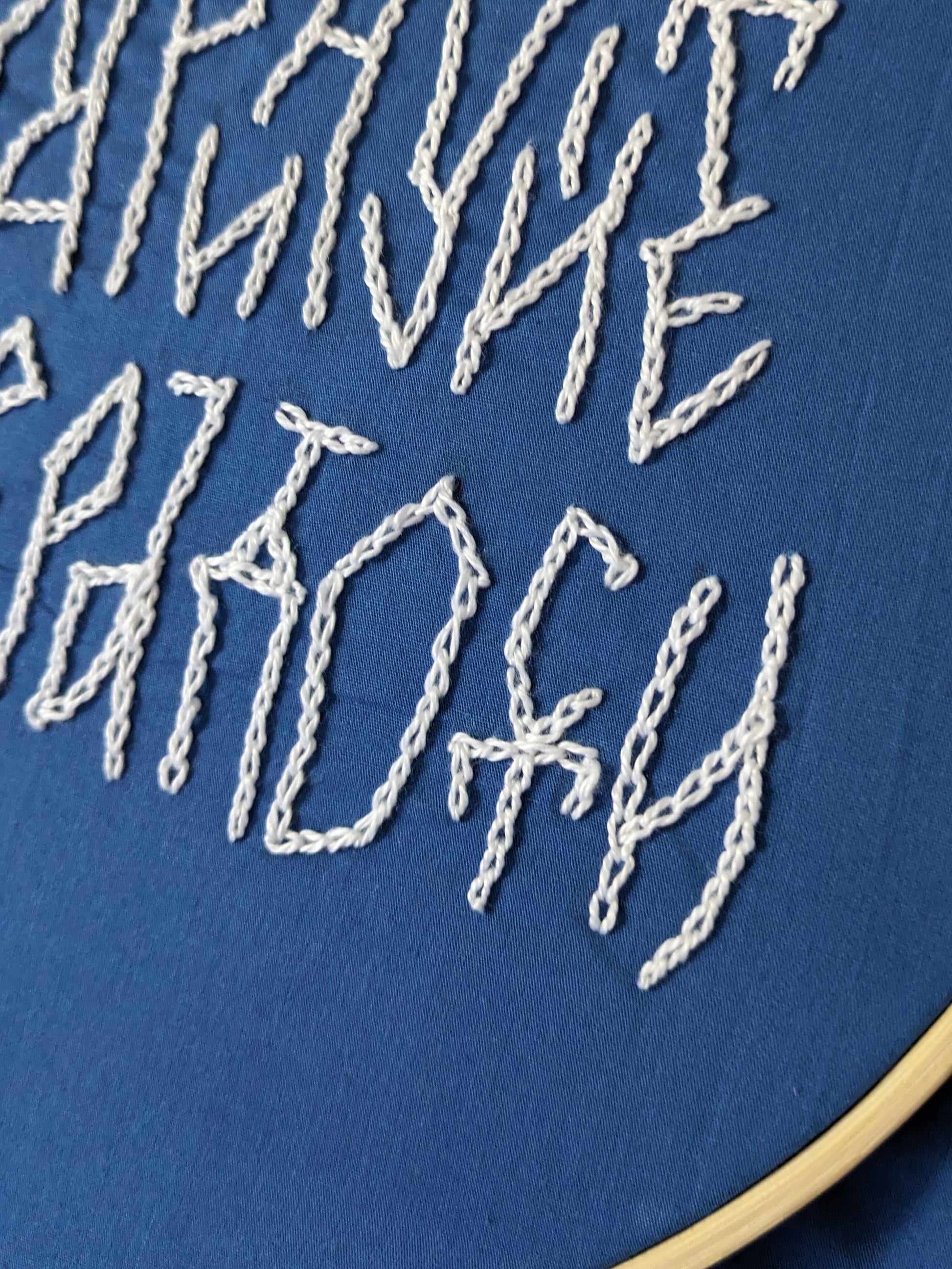 Photo of the part of embroidery lettering. Cyrillic phrase. Blue fabric, white letters