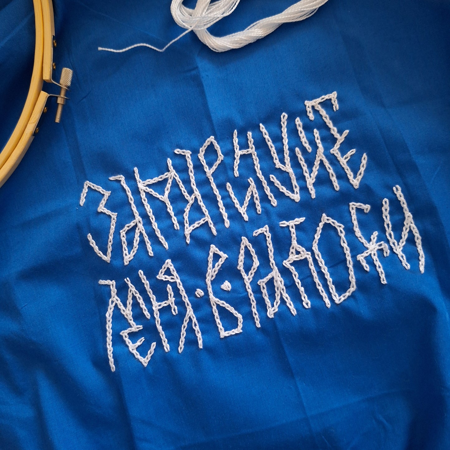 Photo of the whole embroidery lettering. Cyrillic phrase. Blue fabric, white letters