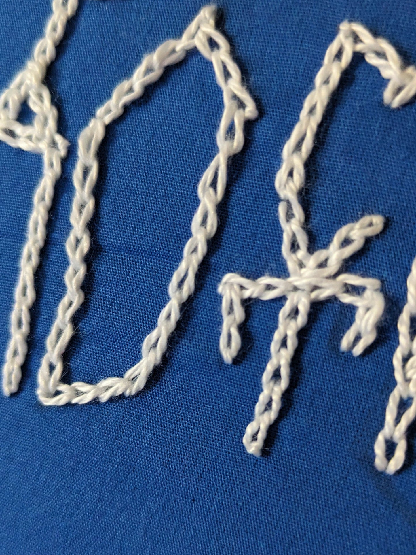 Closeup of embroidery lettering. Cyrillic phrase. Blue fabric, white letters